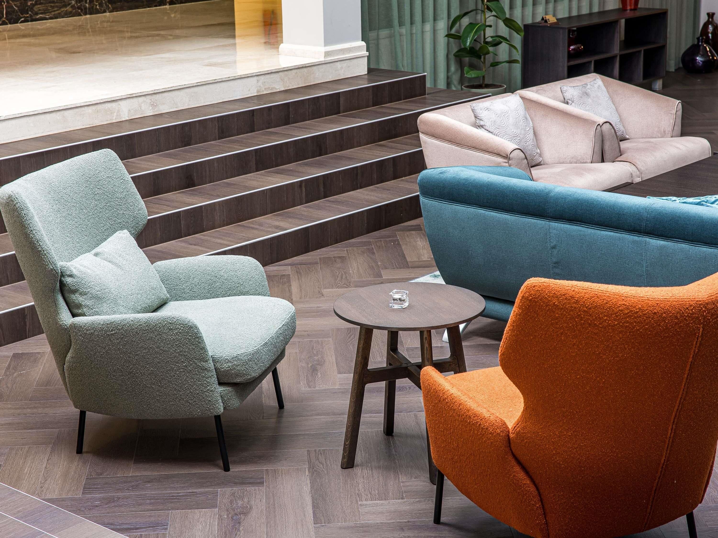 Un hall d’entrée moderne avec un fauteuil vert, un canapé bleu et un fauteuil orange.