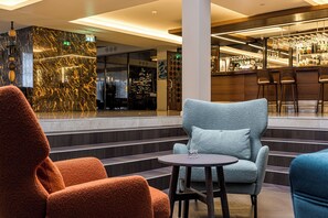 A lobby with a bar area, seating with a round table, and a staircase leading to an upper floor. - Mercure Palanga Vanagupe Resort (Palanga)
