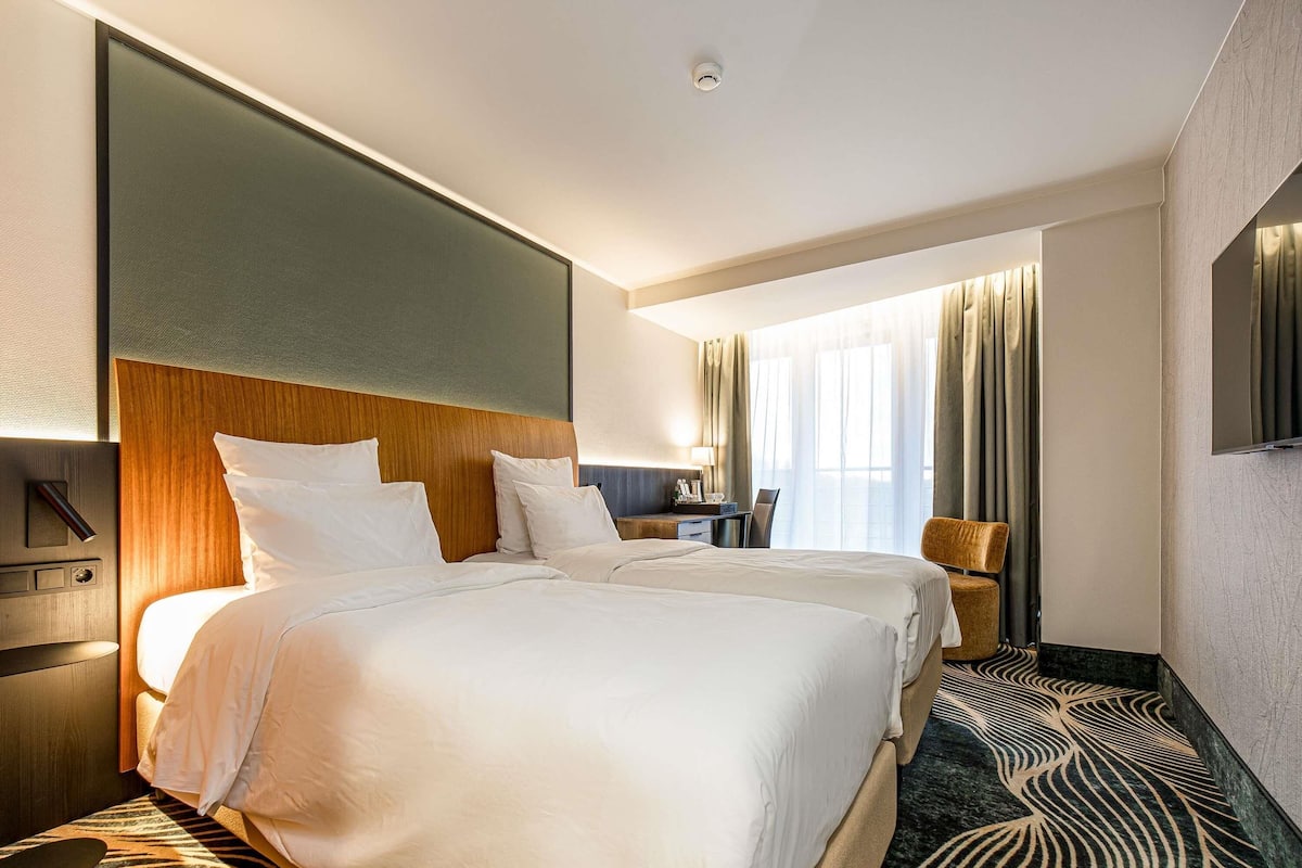 A hotel room with two beds, a desk, a chair, and a TV.