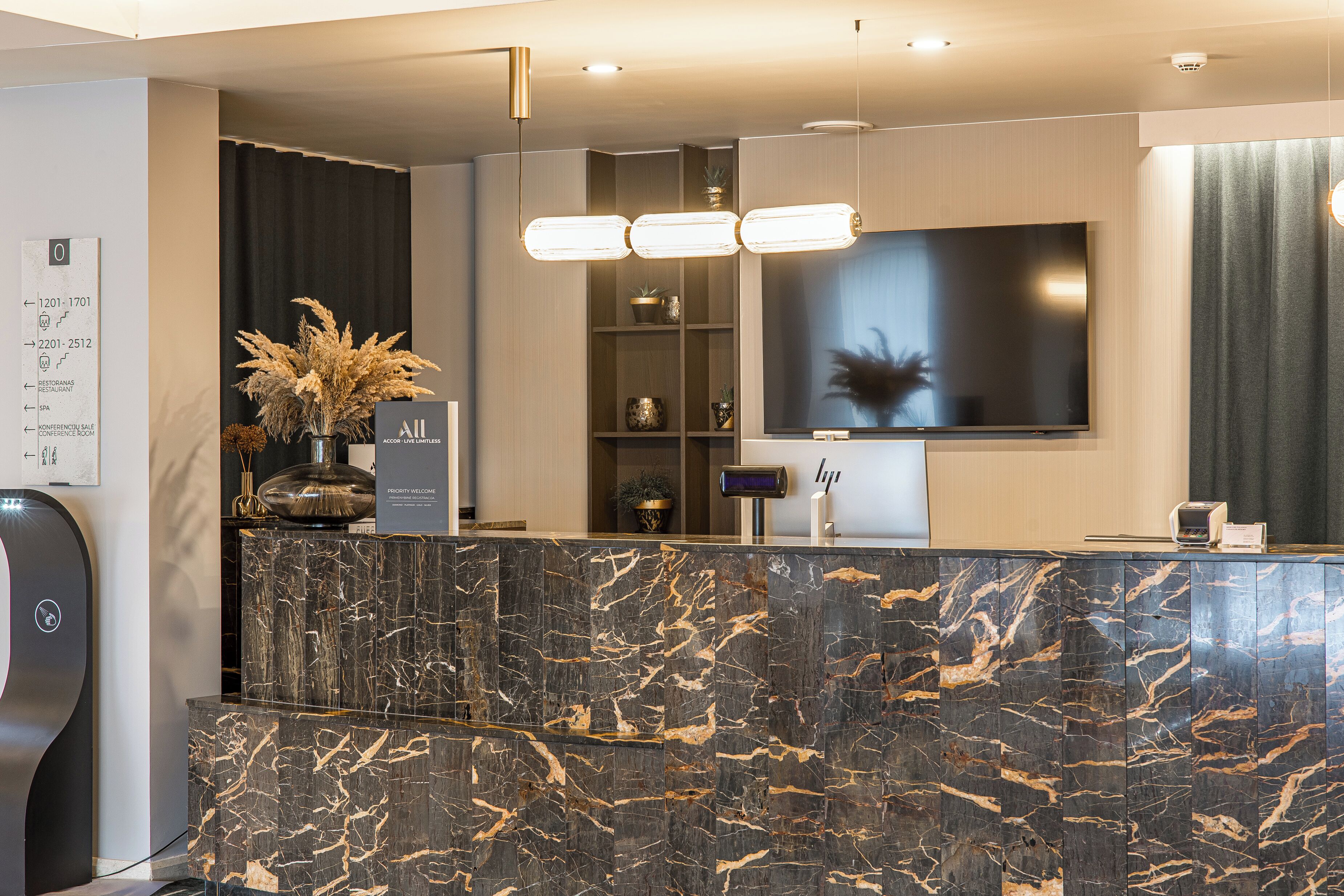 A modern reception area with a marble counter, a flat-screen TV, and a potted plant.