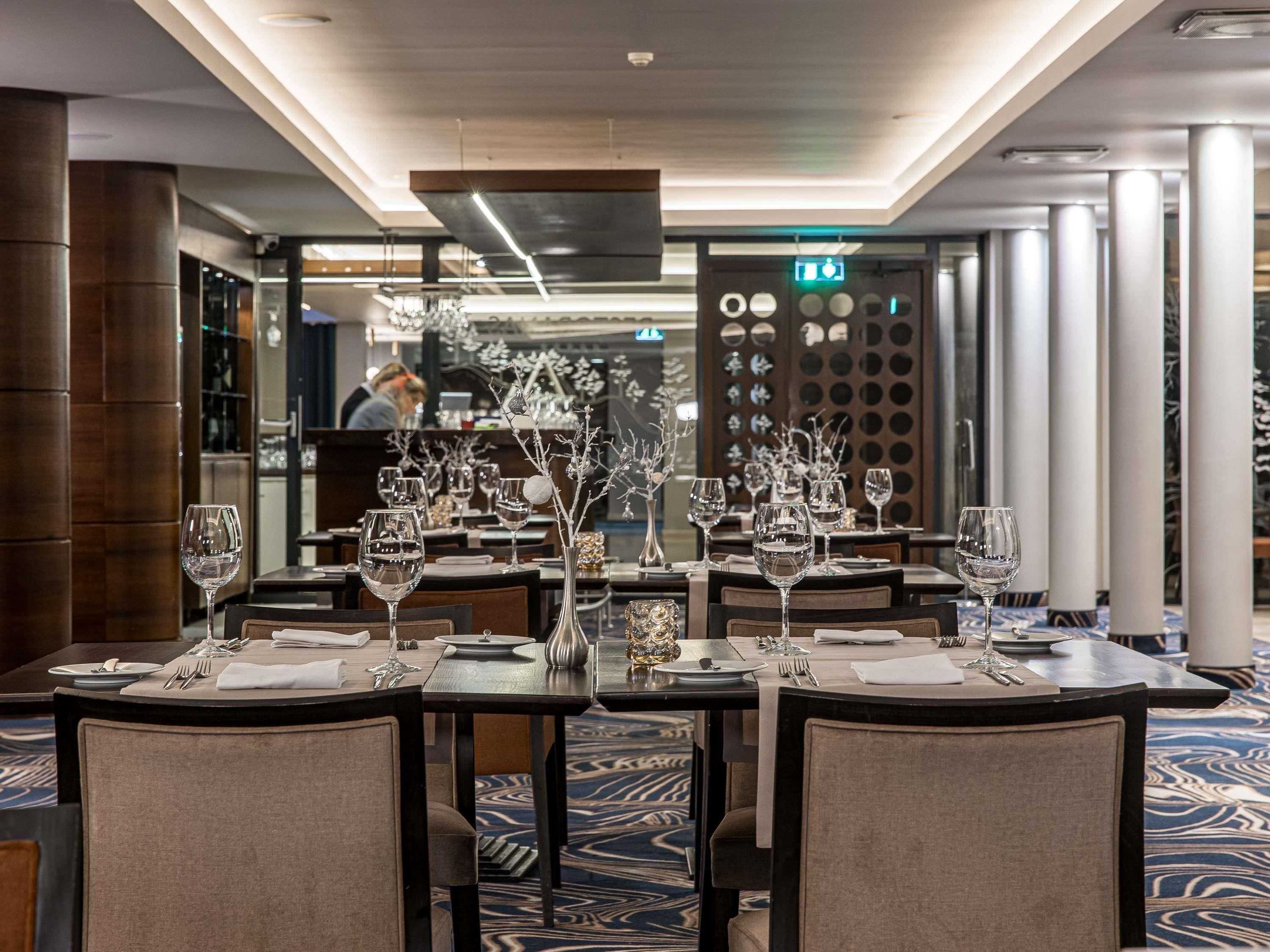 A restaurant with tables set for dining, a modern ceiling design, and a patterned carpet.