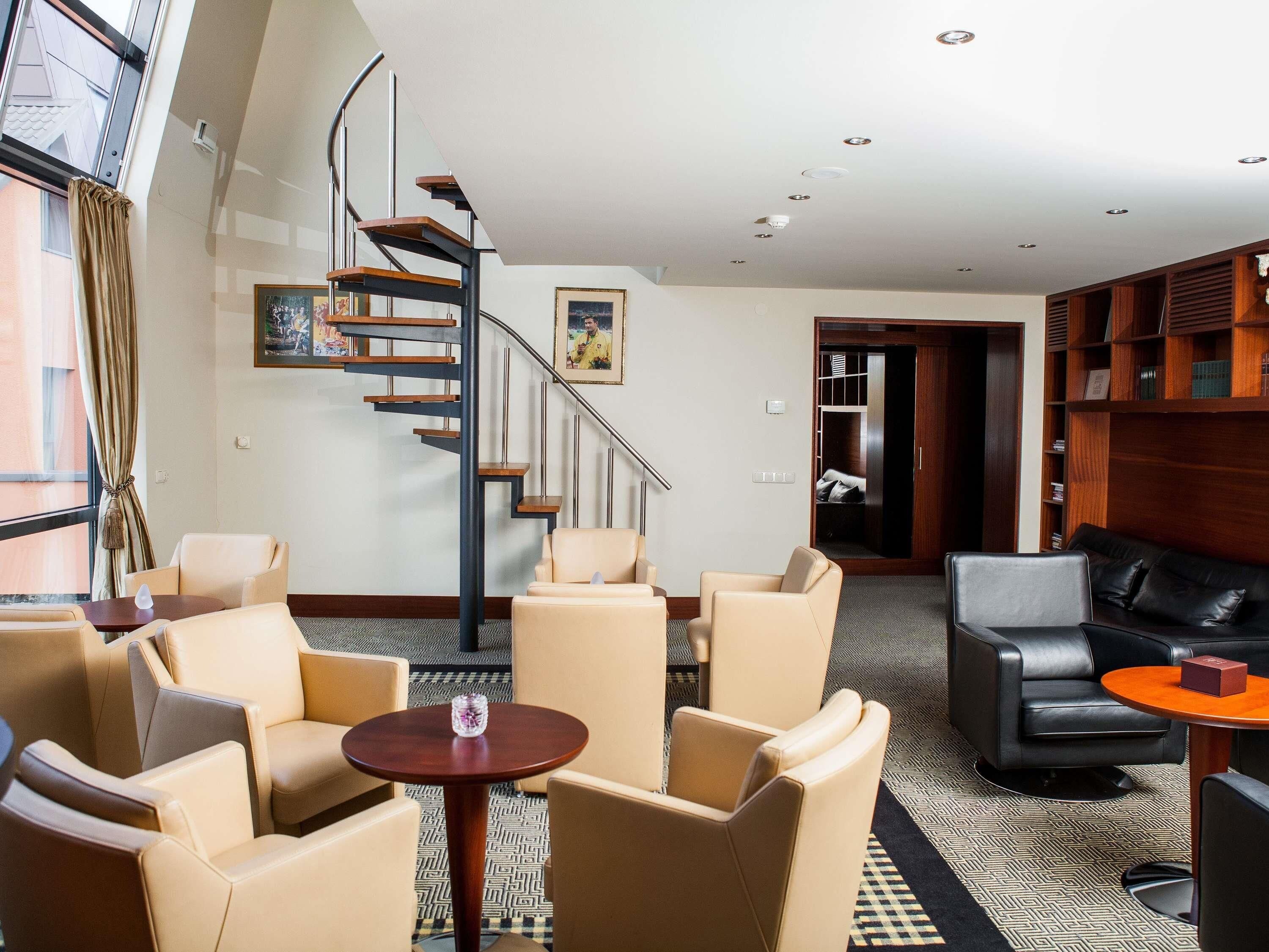 A hotel lobby with a spiral staircase, leather seating, a small table with a vase, and a bookshelf.