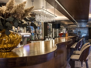 A bar area with a curved counter, a large golden decorative bowl, and a wall-mounted TV. - Mercure Palanga Vanagupe Resort (Palanga)