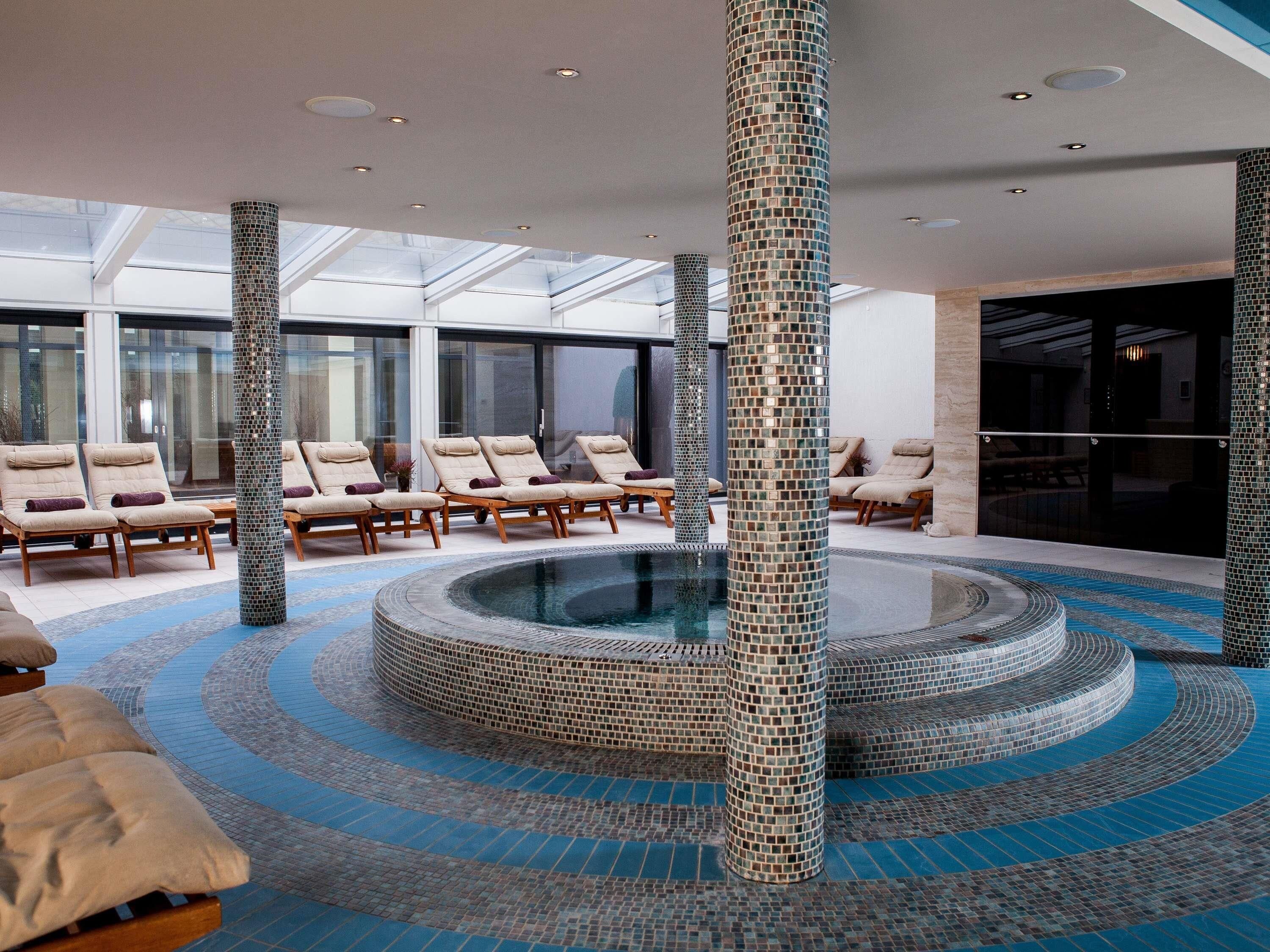 Un espace de bien-être comprenant un jacuzzi circulaire, des chaises longues et un plafond en verre.