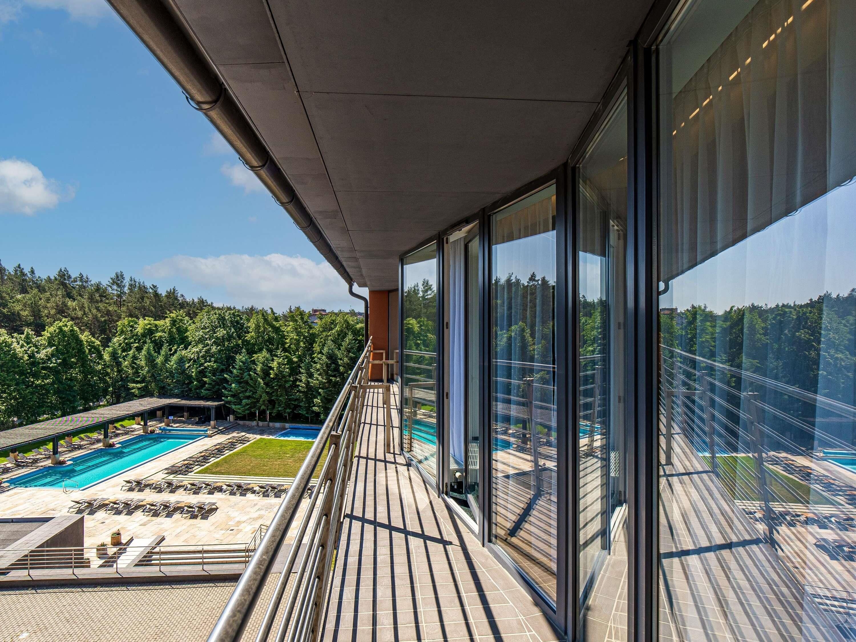 A modern building with a balcony overlooking a swimming pool and a forested area.