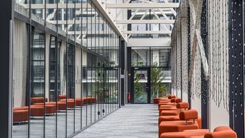 A modern interior with glass walls, orange seating, and a geometric ceiling structure.