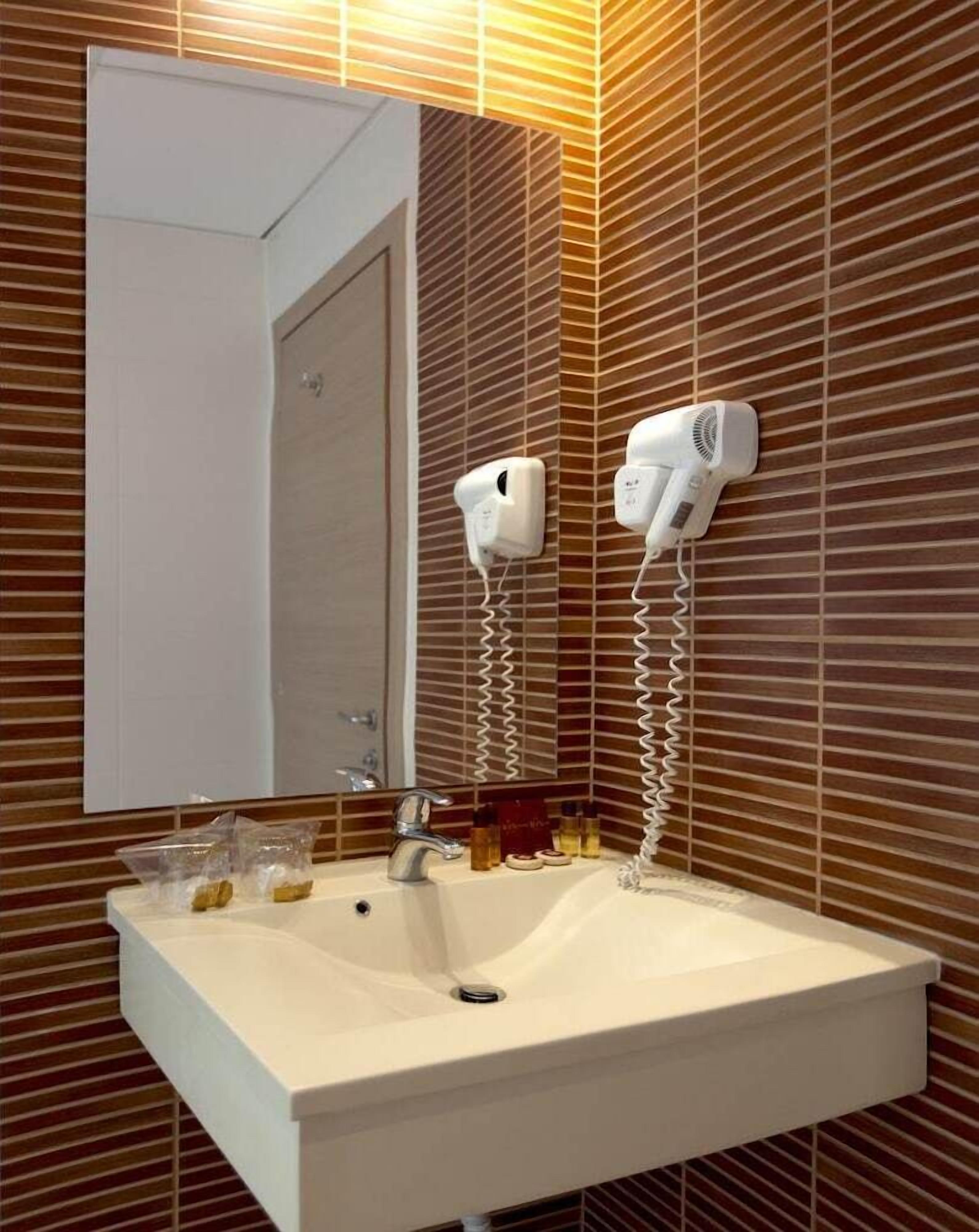 A bathroom with a white sink, a mirror, and two hair dryers mounted on the wall.