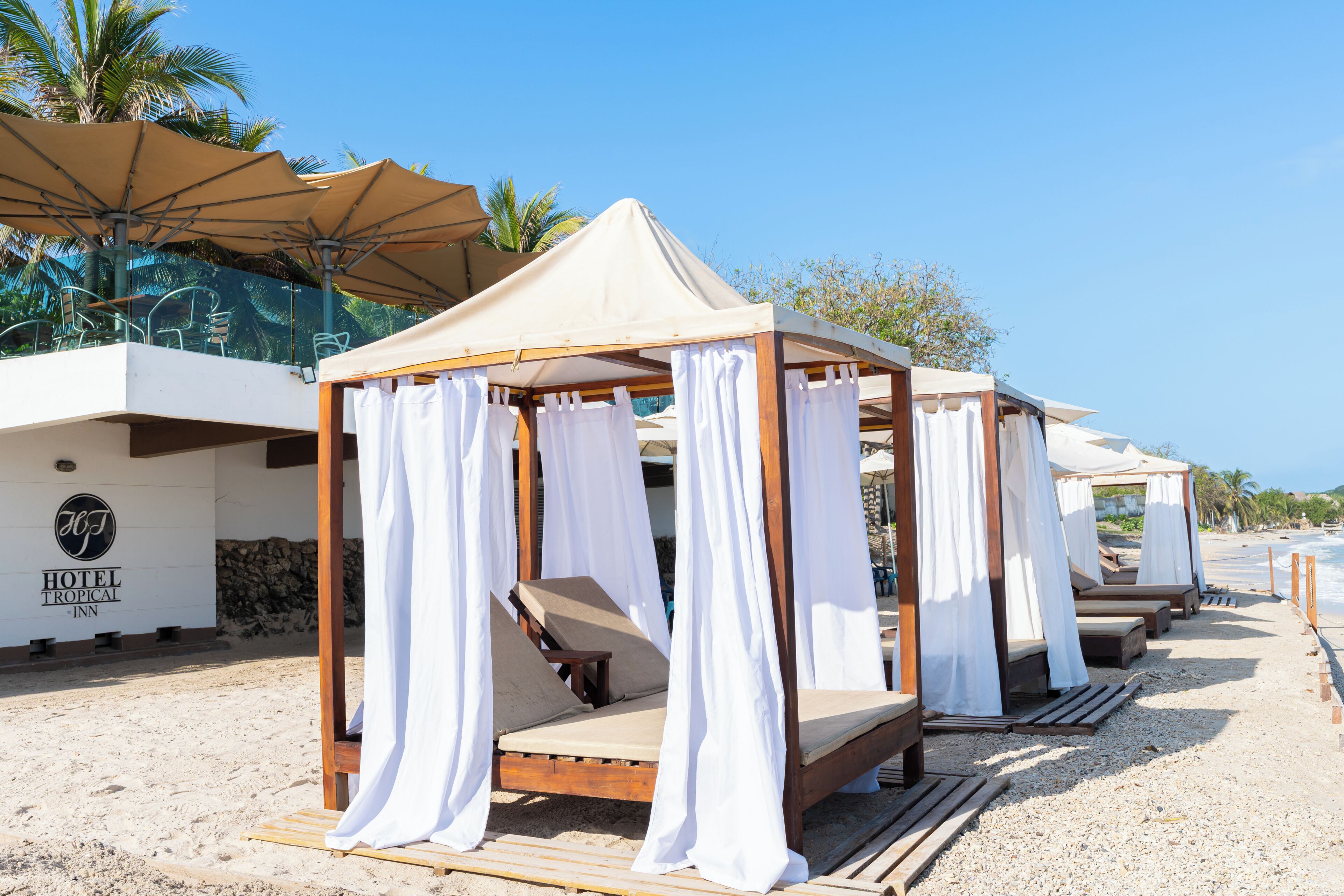 Ein Hotel am Strand mit Holzbungalows, weißen Vorhängen und blauem Himmel.