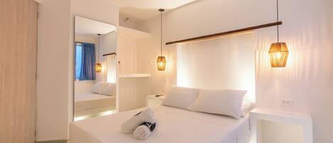 A modern hotel room with a large bed, bedside tables, a mirror, and pendant lighting.