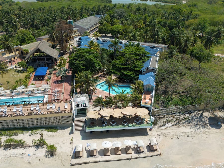 An aerial view of a hotel with a swimming pool, beach area, and surrounding tropical vegetation.