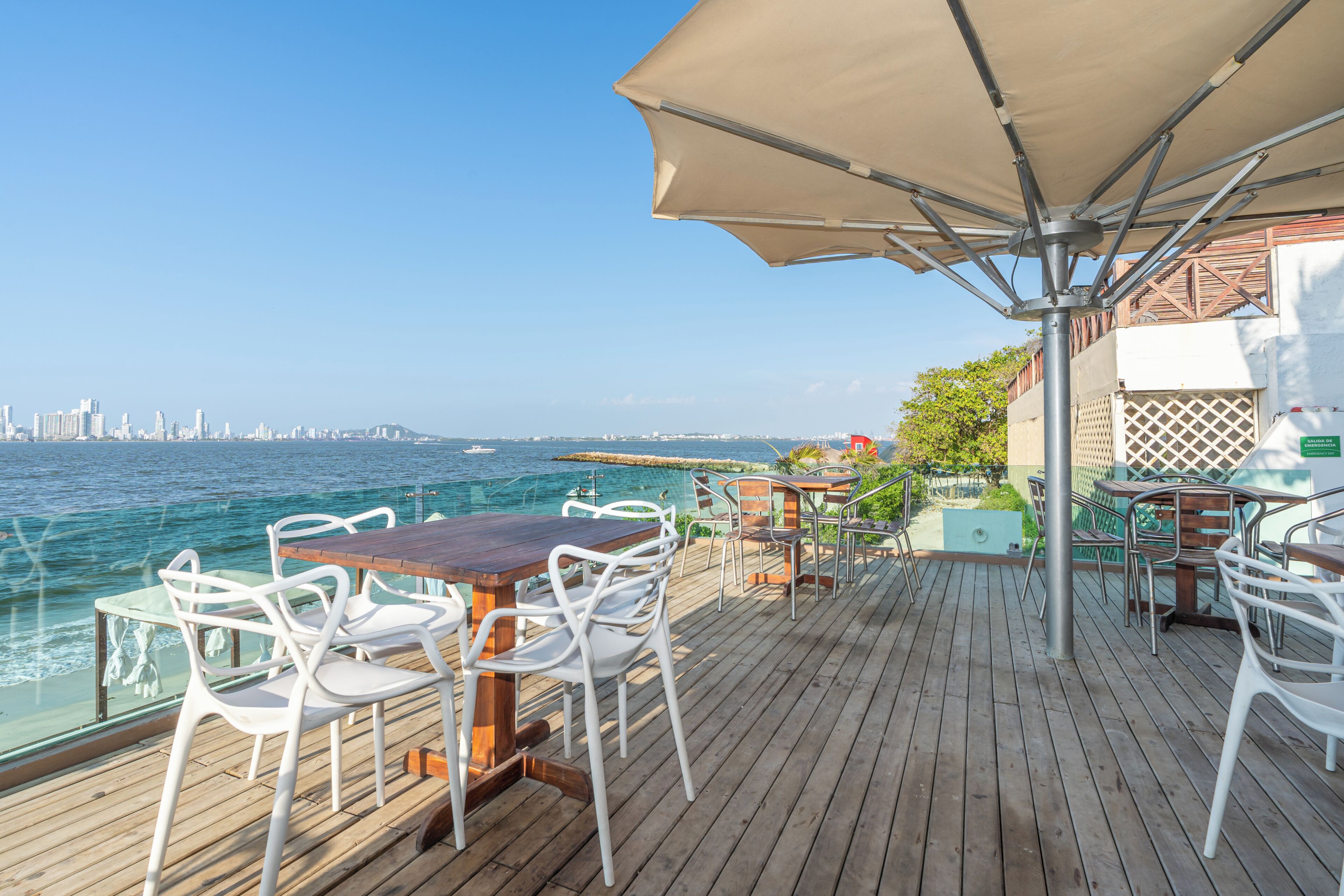 Une terrasse en bois avec des sièges extérieurs, une vue sur l’océan et, au loin, le panorama de la ville.