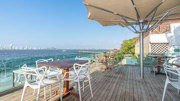 Une terrasse en bois avec des sièges extérieurs, une vue sur l’océan et, au loin, le panorama de la ville.