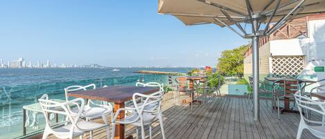 Um deck de madeira com área de estar externa, vista para o oceano e um horizonte urbano ao longe.