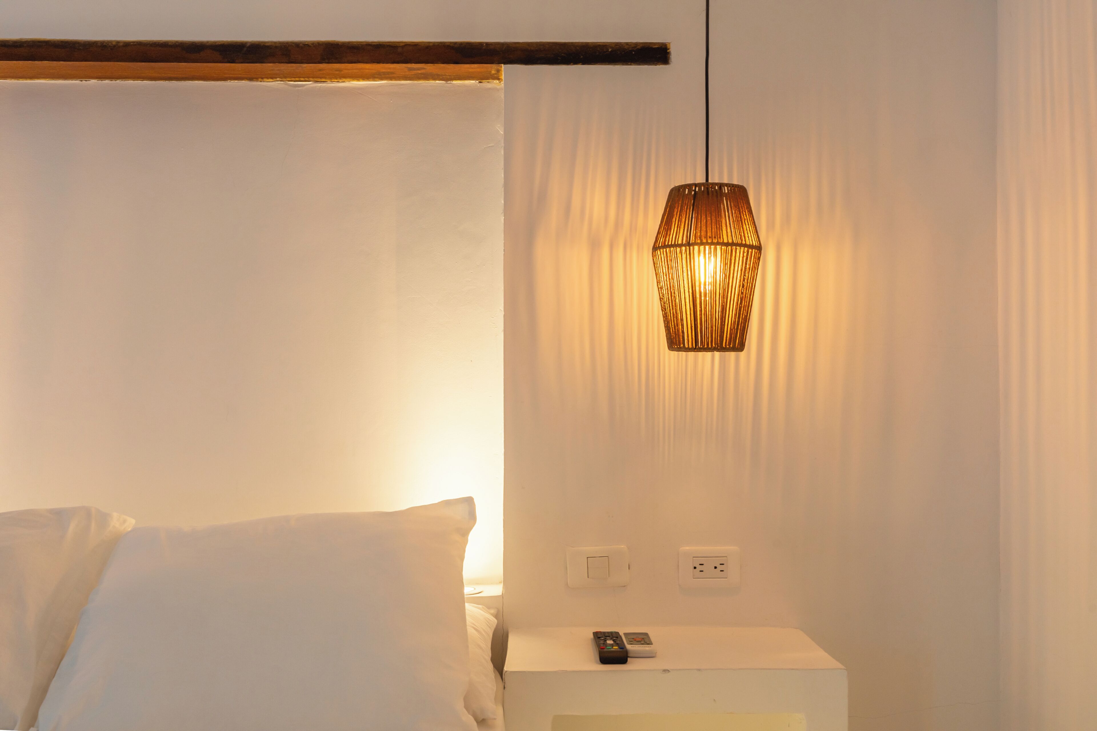 Ein Schlafzimmer mit einem Bett, einem Nachttisch mit Fernbedienung und einer Hängelampe.