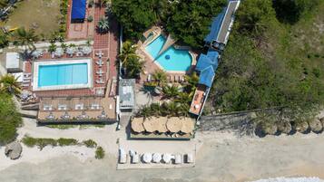 An aerial view of a resort with a large swimming pool, sun loungers, and a beach area.