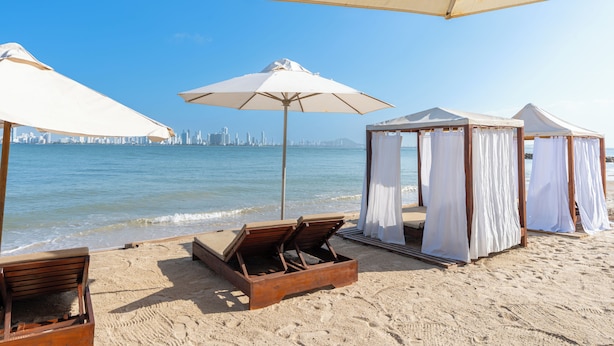 A beach with lounge chairs, umbrellas, and a city skyline in the background. - Hotel Tropical Inn (Cartagena)