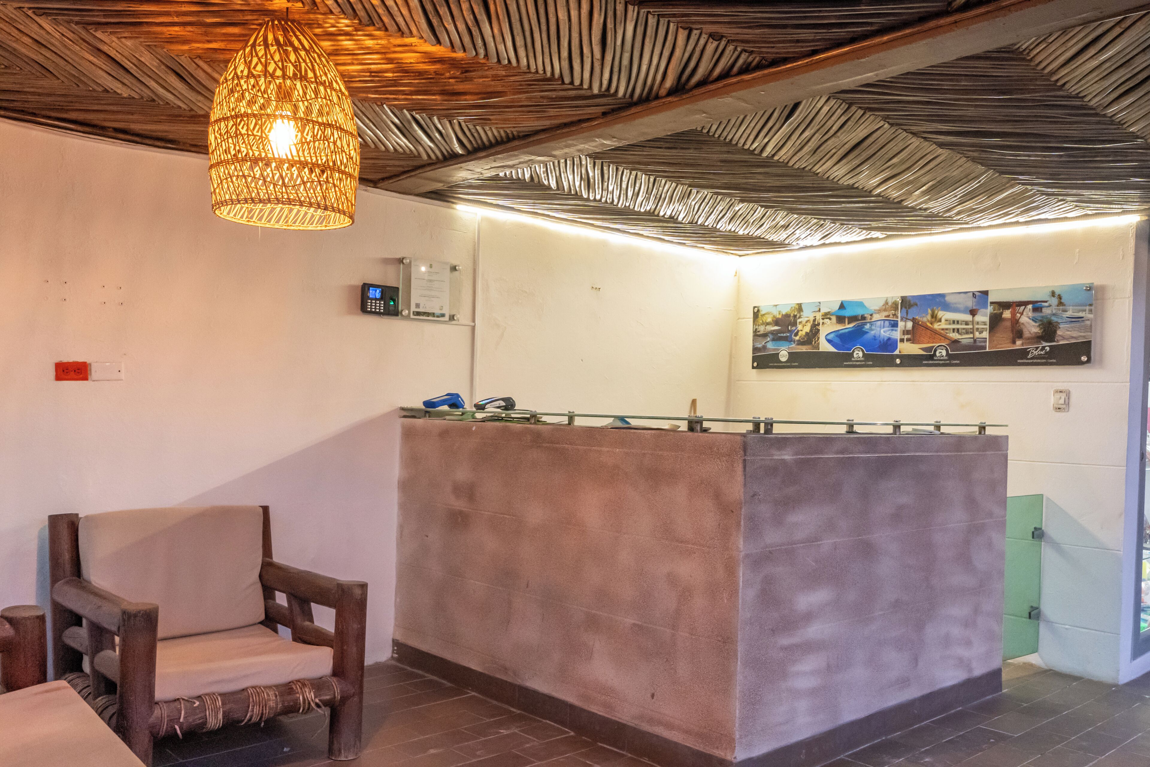 Un área de recepción con una silla de madera, un mostrador de recepción, una lámpara colgante y un termostato fijado a la pared.