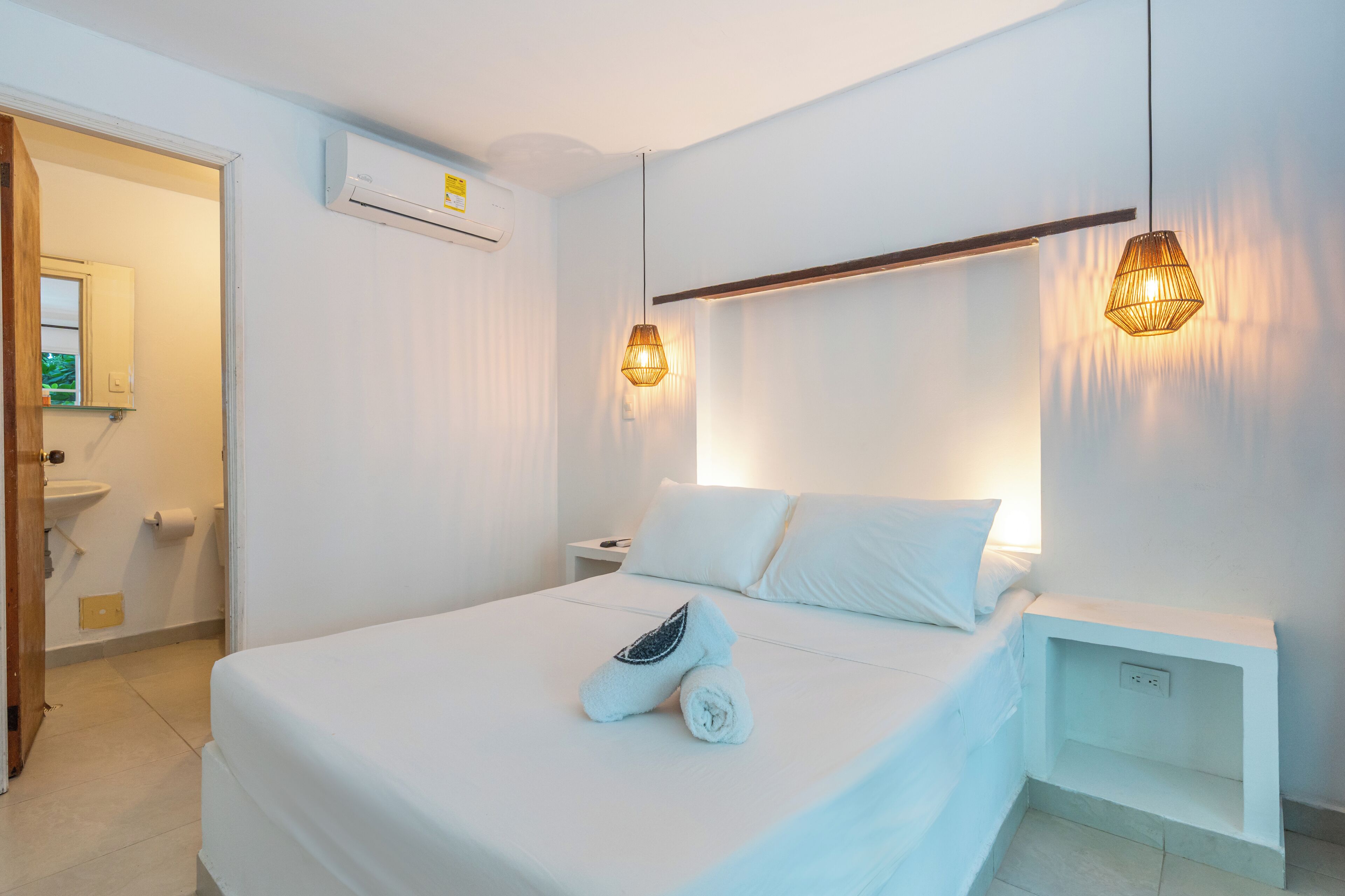 Een hotelkamer met een bed, nachtkastjes, een airconditioner en hanglampen.