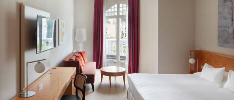 A hotel room with a bed, desk, chair, and a small table.