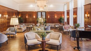 A spacious lobby with a grand chandelier, wooden paneling, and a grand piano.