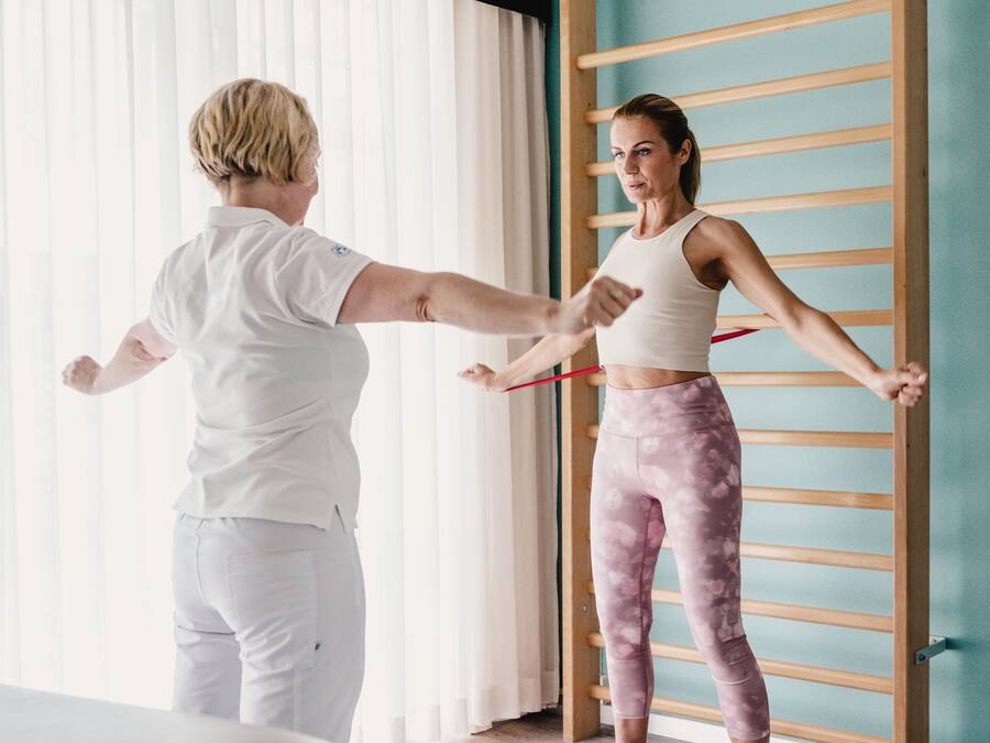 A person stretching with a resistance band in a room with a wooden rack and a window with blinds.