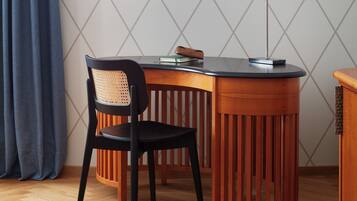 A corner room with a wooden desk, a black chair, a lamp, and a patterned wall.