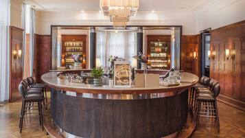 A bar area with a round counter, bar stools, a chandelier, bookshelves, and a wooden floor.