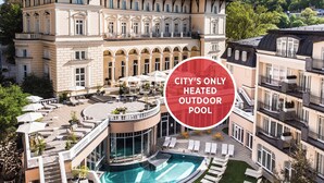 A luxurious outdoor pool area with multiple lounge chairs and umbrellas, surrounded by classical architecture.