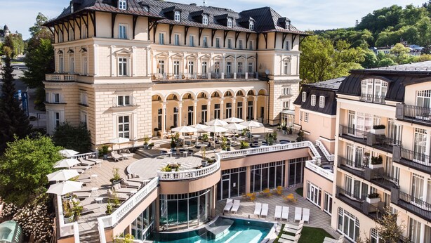 A large, multi-story hotel with a pool area, outdoor seating, and a view of the surrounding landscape.