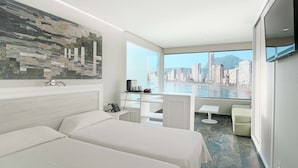 A modern hotel room with two beds, a city view, a dining area, and a large window. -  KAKTUS Hotel Benikaktus (Benidorm)