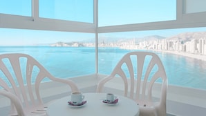 A room with a large window overlooking a coastal city and ocean. There are two white chairs and a small table with two cups of coffee. -  KAKTUS Hotel Benikaktus (Benidorm)