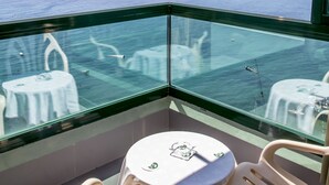 A balcony with a glass railing, two white plastic chairs, and a small round table with a green logo. -  KAKTUS Hotel Benikaktus (Benidorm)