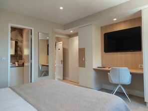 A modern hotel room with a bed, a desk, a chair, a TV, and a wardrobe.