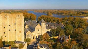 A historic stone building with a prominent tower, surrounded by trees and a river.