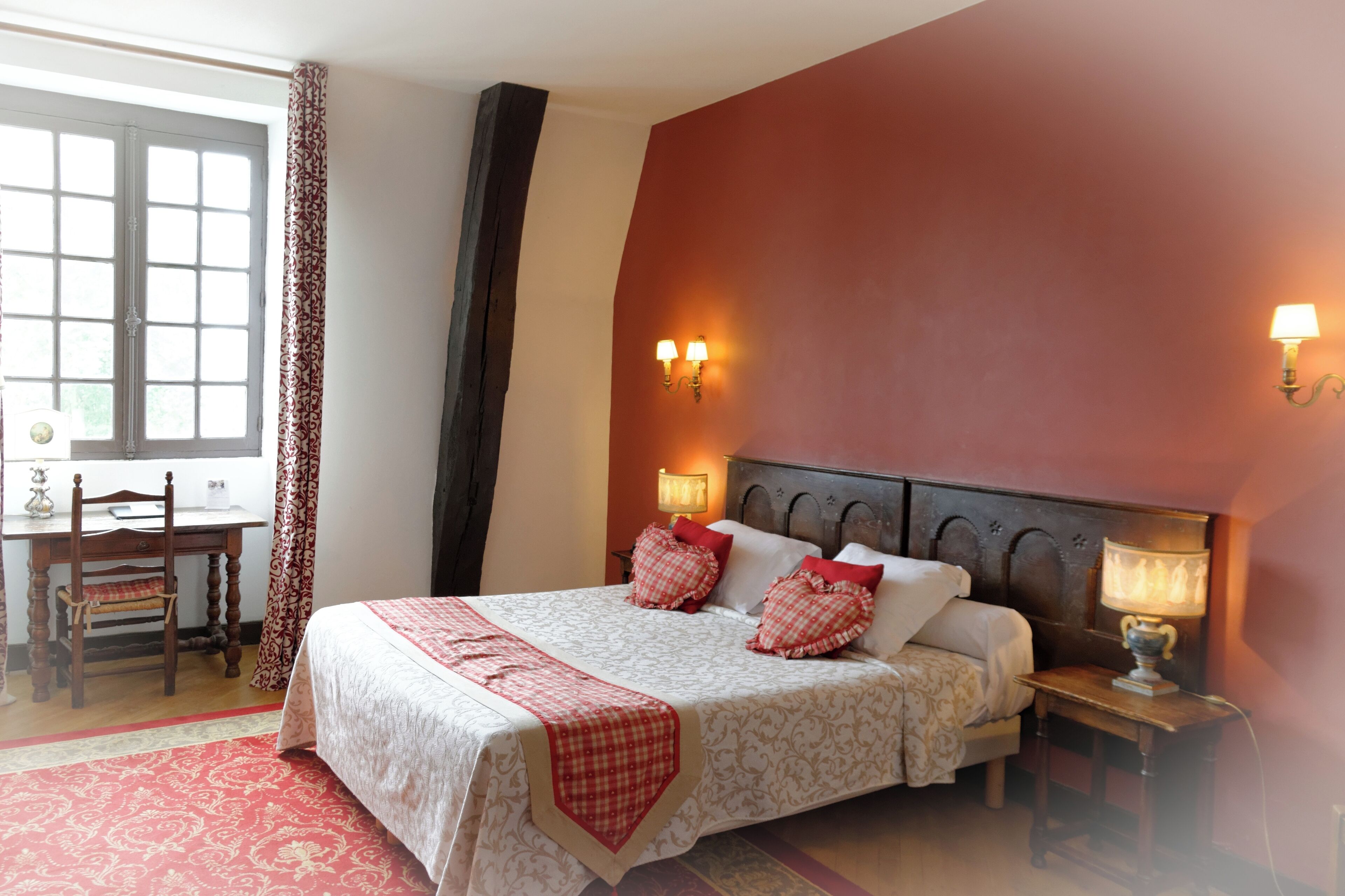 Een slaapkamer met een groot bed, twee bedlampjes, een bureau met stoel, en een raam met gordijnen.