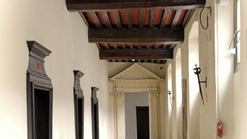 A corridor with a tiled floor, wooden beams on the ceiling, and black-framed doors.