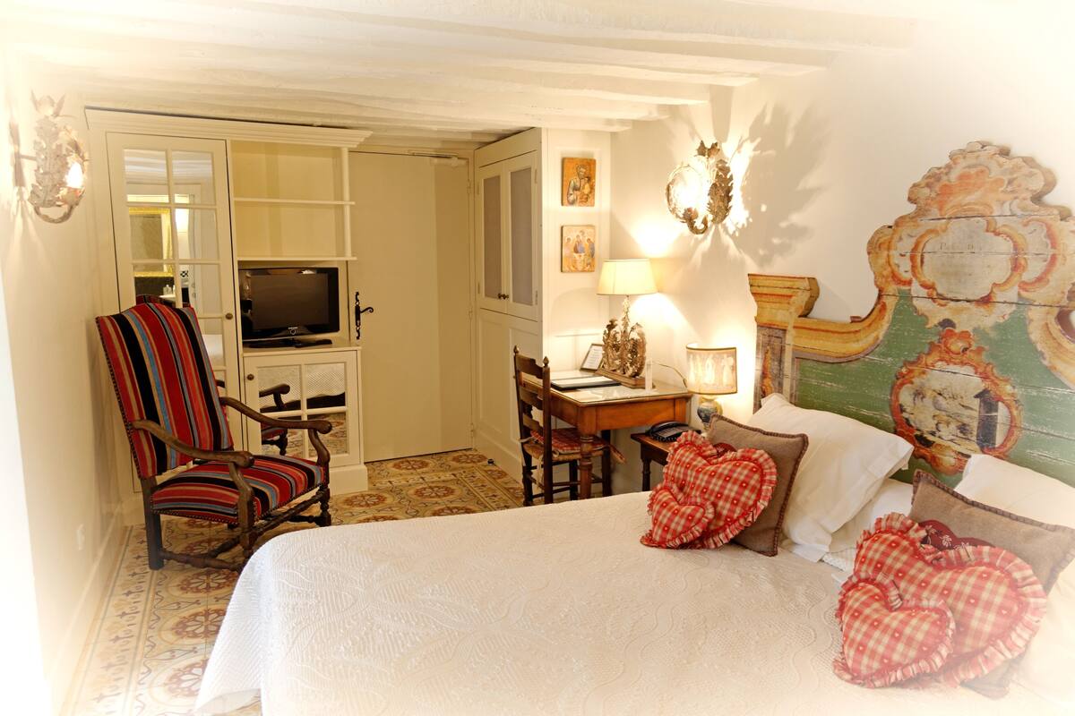 A hotel room with a bed, a television, a desk with a lamp, a chair, and a decorative wall.