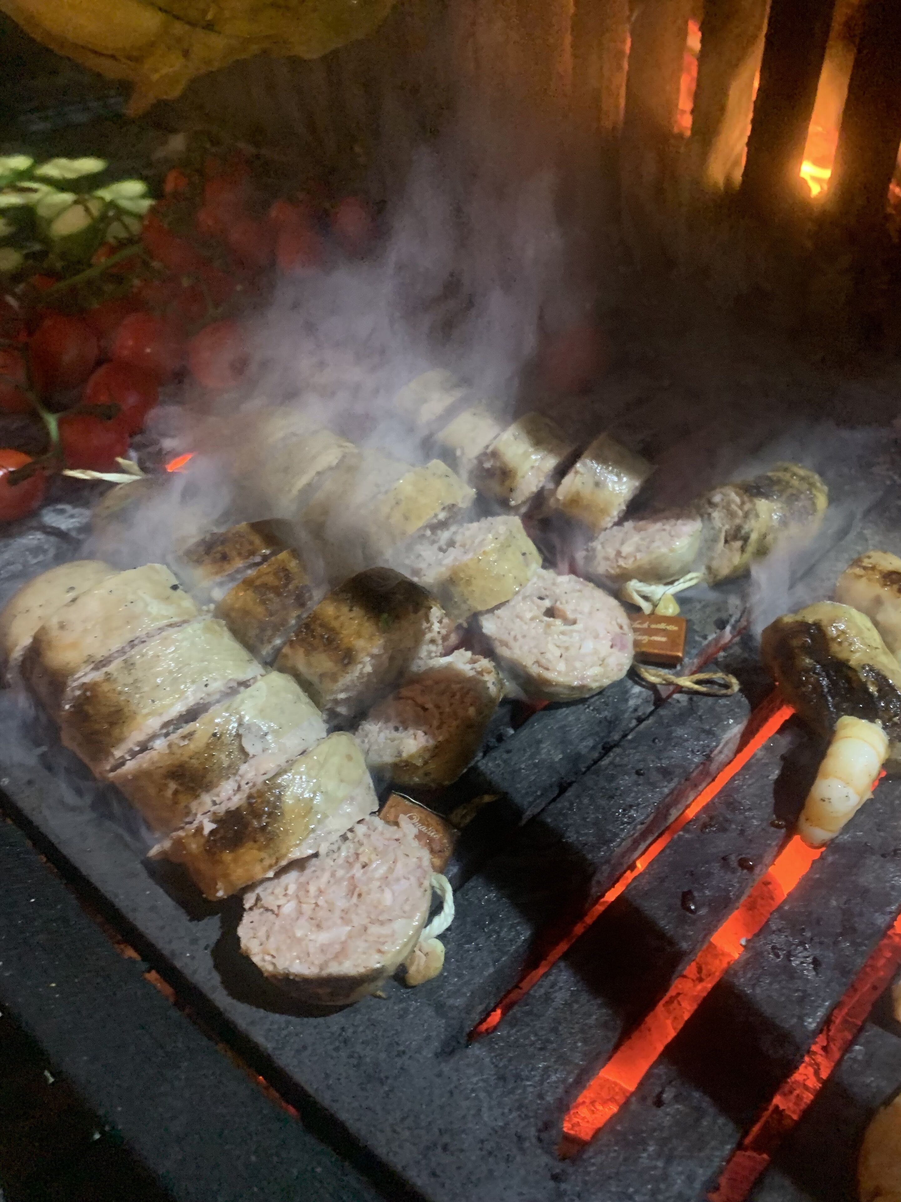A grill with various meats and vegetables being cooked over charcoal.