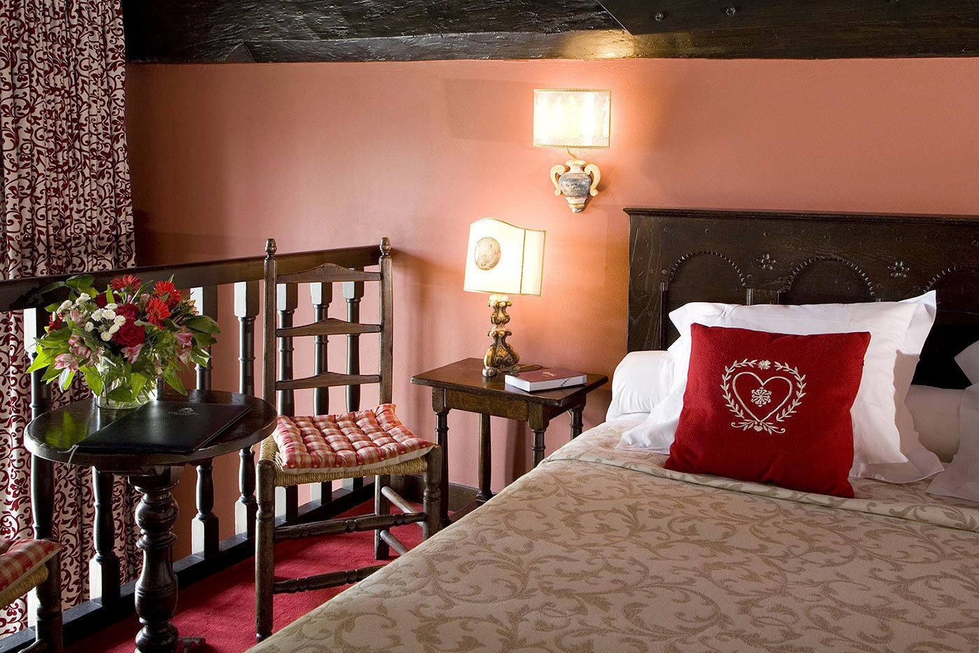 Hotelkamer met een bed, een stoel, een tafel met bloemenvaas en een wandlamp.