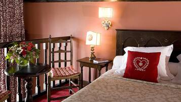 Hotelkamer met een bed, een stoel, een tafel met bloemenvaas en een wandlamp.