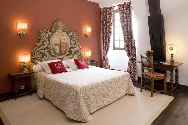 Un dormitorio con una cama grande, dos lámparas de noche, un cabecero decorativo, una silla de madera y un escritorio con lámpara.