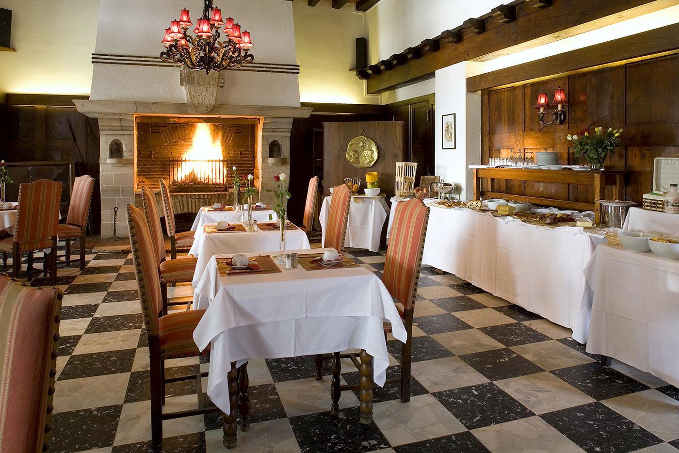 Un comedor con mesas dispuestas para una comida, una chimenea y una araña.