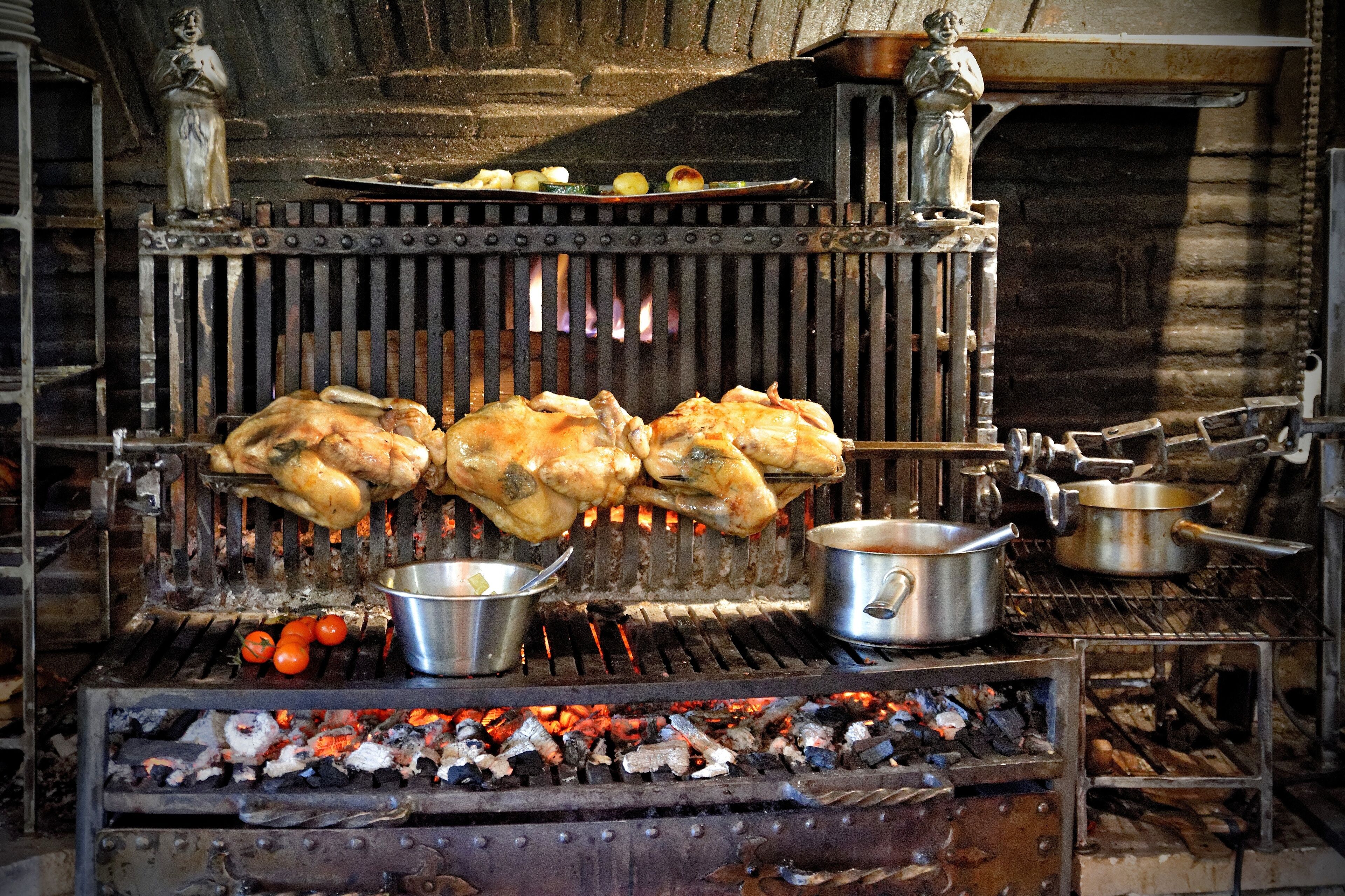 Ein traditionelles Kochgelände im Freien mit Grill, Töpfen und rustikalem Holz im Hintergrund.