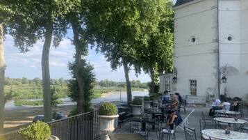 An outdoor cafe with tables and chairs, overlooking a river and surrounded by trees.