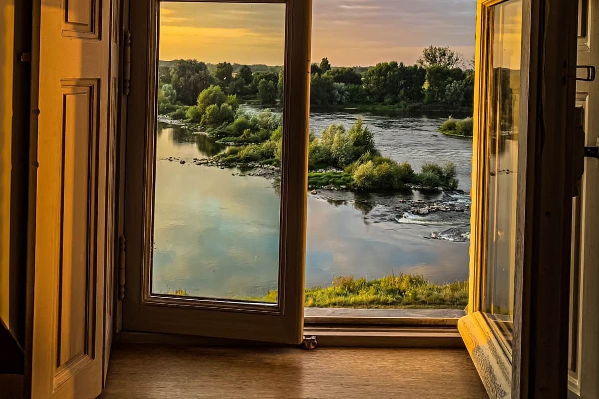 An open door leading to a view of a river and greenery.