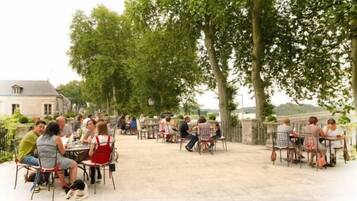 Café al aire libre con mesas y sillas dispuestas bajo árboles, con vistas a un cuerpo de agua.