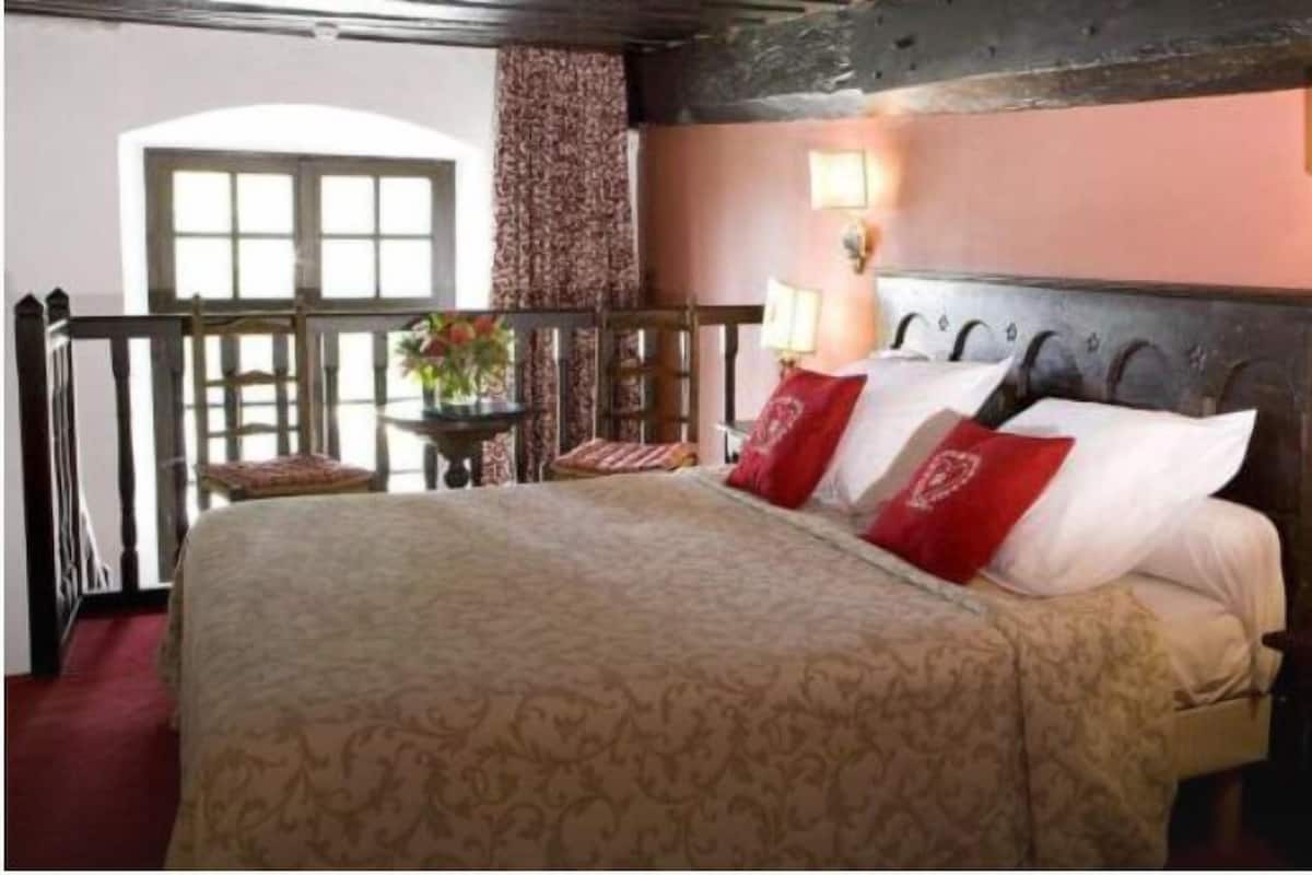 A bedroom with a large bed, a small table with a vase of flowers, and a balcony with a view of the outside.