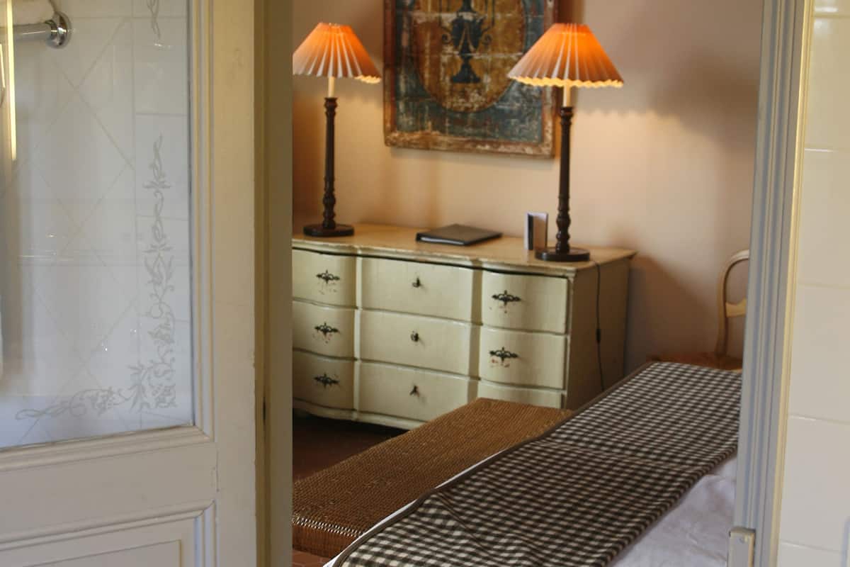 A bedroom with a bed, two bedside lamps, a dresser, and a painting on the wall.