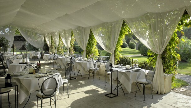 An outdoor dining area with tables set for a meal, surrounded by draped white fabric and greenery. - Le Mas De Peint (Arles)