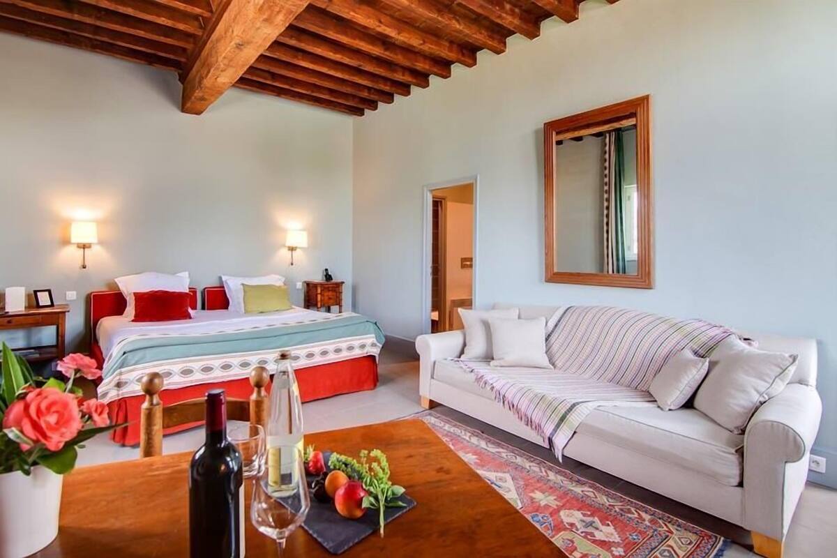 A bedroom with a bed, bedside tables, a sofa, a mirror, and a wooden ceiling.